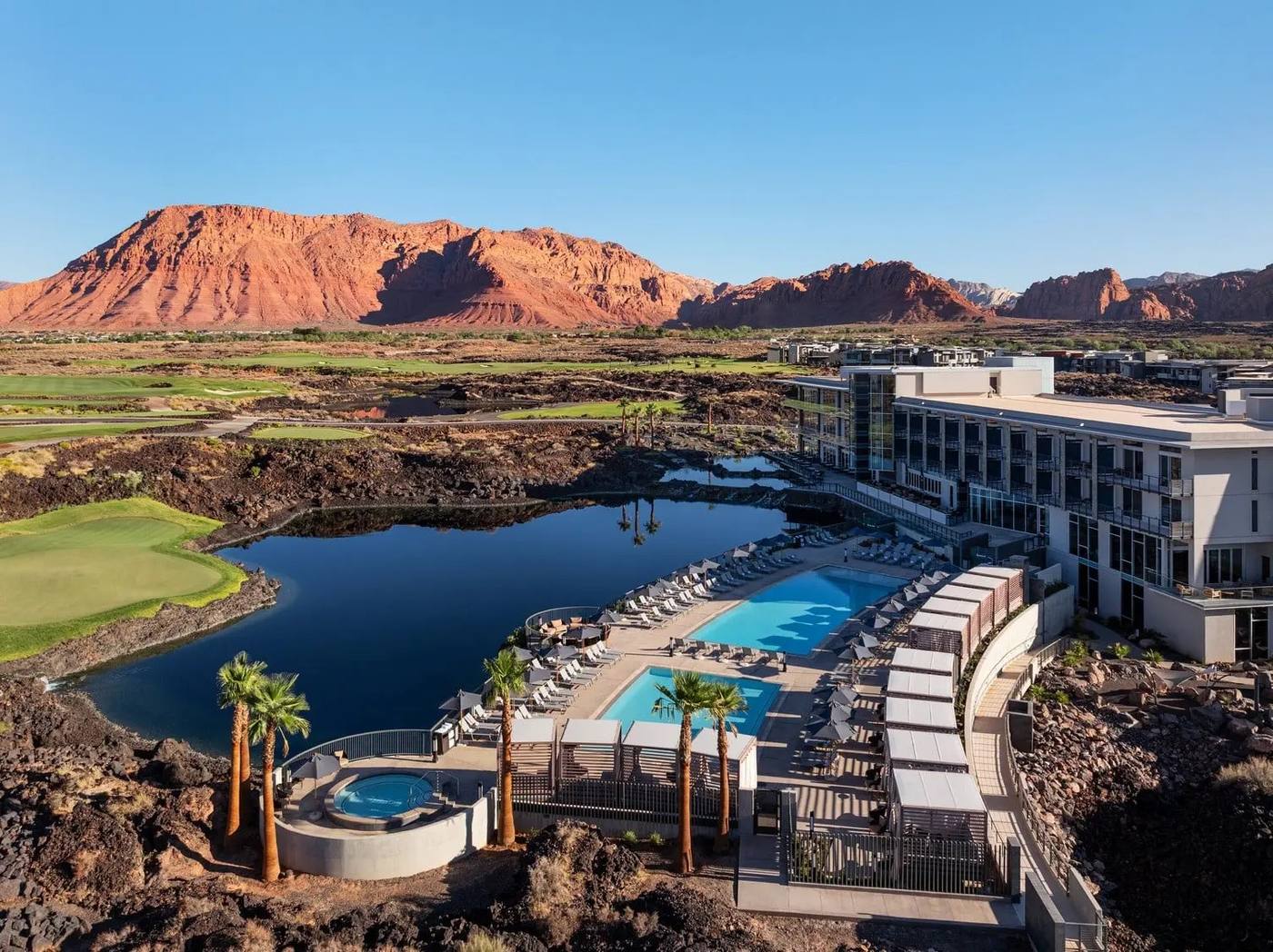 Aerial view of Black Desert Resort, its pools and lake, with the red rock of Greater Zion behind